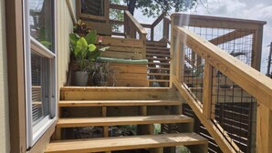 Una escalera de madera con barandilla metálica, rodeada de macetas con plantas.
