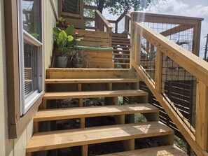 A wooden staircase with a metal railing, surrounded by potted plants.