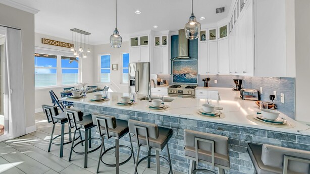 A modern kitchen with a large island, bar stools, pendant lighting, and a view of the ocean.