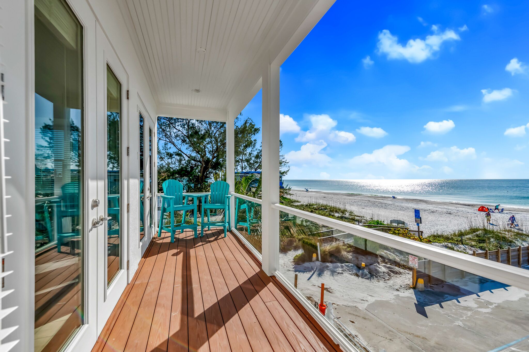 A wooden deck with glass doors and a view of the beach.