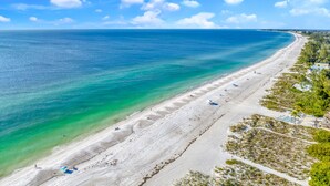 A coastal beach with clear turquoise waters, a sandy shore, and a few umbrellas.