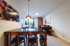 A modern living room with a dining area, a sofa, a TV, and artwork on the walls. - VG Sun Cumbuco Pé Na Areia Bangalô 6 Pessoas By DM Apartments (Caucaia)