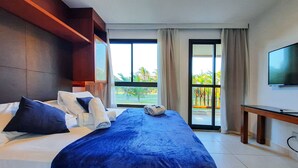 A hotel room with a large bed, a TV, and a balcony with a view of palm trees. - VG Sun Cumbuco Pé Na Areia Bangalô 6 Pessoas By DM Apartments (Caucaia)
