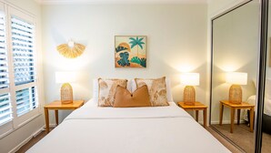 Habitación de hotel con una cama, dos mesitas de noche con lámparas, una obra de arte en la pared y una ventana con persianas.