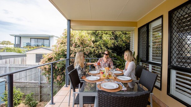 Un área de comedor al aire libre con un porche cubierto, barandales de metal y vistas a casas vecinas.