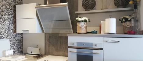 A modern kitchen with white cabinetry, a built-in oven, and a countertop with a kettle and a coffee maker.