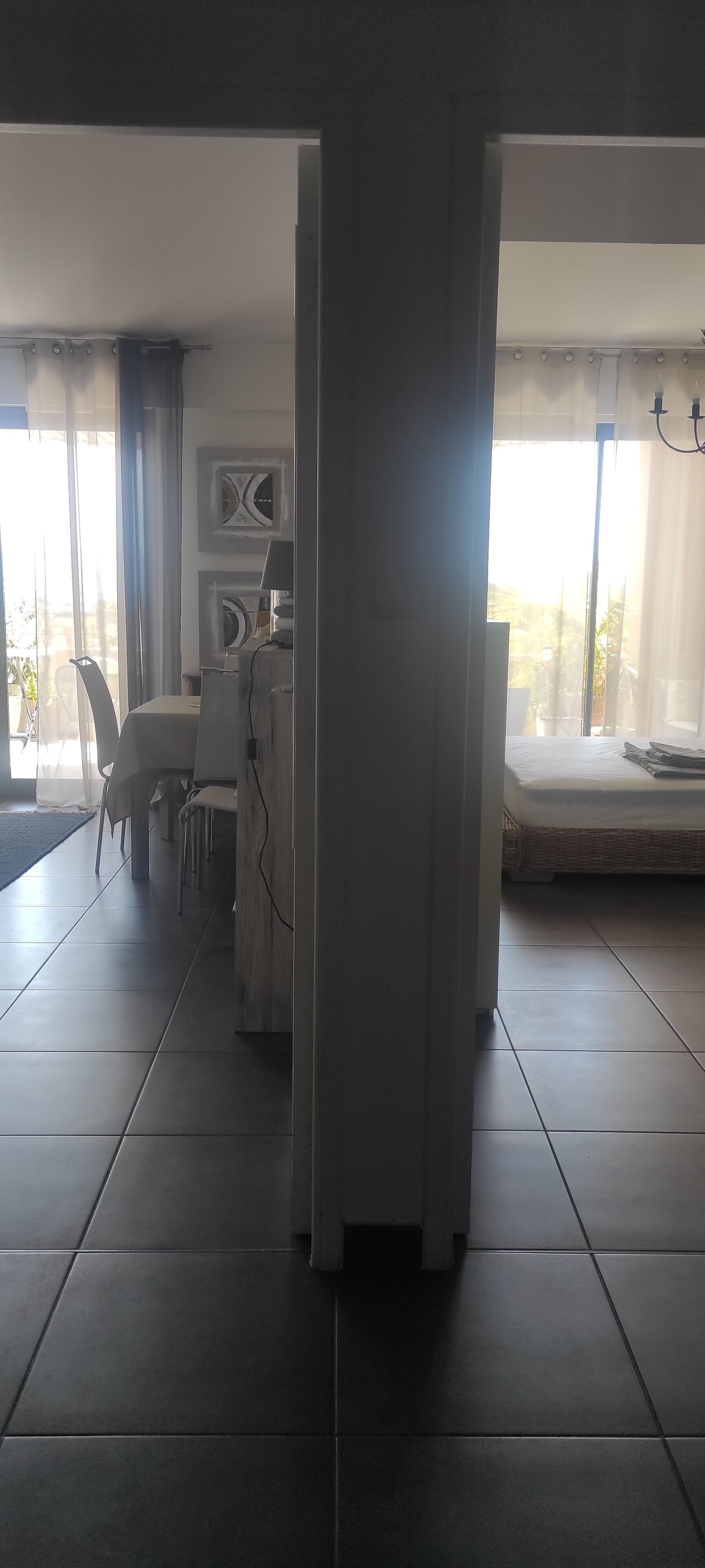 A modern living room with a dining area, large windows with sheer curtains, and a view of the outdoors.
