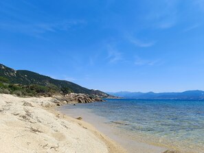 A beach with clear water, rocky shoreline, and mountains in the background.