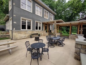 A patio with a round table and chairs, a stone wall, and a covered seating area with a pergola.