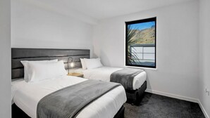 Een moderne hotelkamer met twee bedden, een groot raam met uitzicht op een bergachtig landschap, en een minimalistisch design.