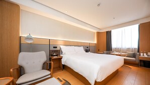 A hotel room with a large bed, a seating area with a table, and a desk with a computer.