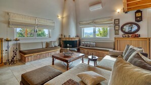 A cozy living room with a fireplace, wooden beams, and a large window.