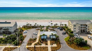 Un hôtel situé en bord de mer, avec un parking, une plage en arrière-plan et un ciel dégagé.