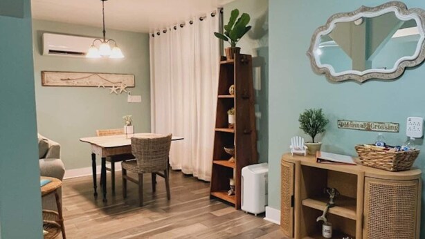 Een eetgedeelte met een tafel, stoelen, een boekenkast, een spiegel en een plafondventilator.