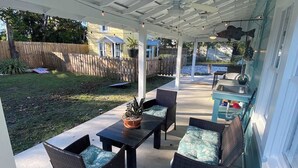 Een terras buiten met een overdekte zithoek, een tafel en stoelen.