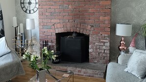 A living room with a brick fireplace, a round clock, and a sofa. - Morecambe Apartment - Sleeps 3 - 5 Mins to Sea (Morecambe)