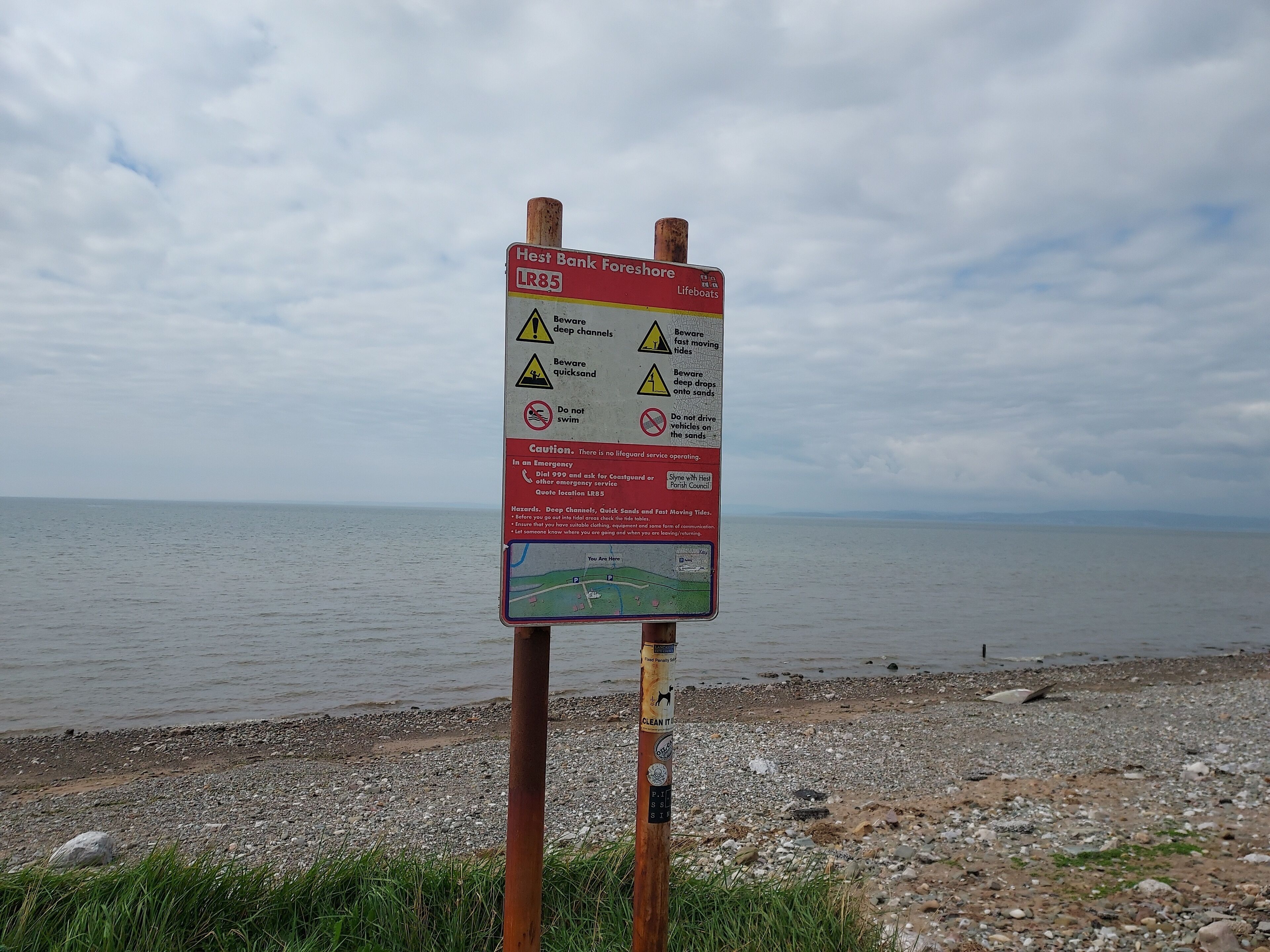 A warning sign with safety instructions near a beach.