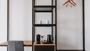 A modern, compact room with a wooden desk, a grey chair, and a black coffee maker. - Step Inn The Fair Hotel (Rosbach vor der Hoehe)
