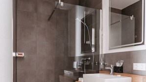 A modern bathroom with a glass-enclosed shower, a white sink, and a wooden vanity. - Step Inn The Fair Hotel (Rosbach vor der Hoehe)