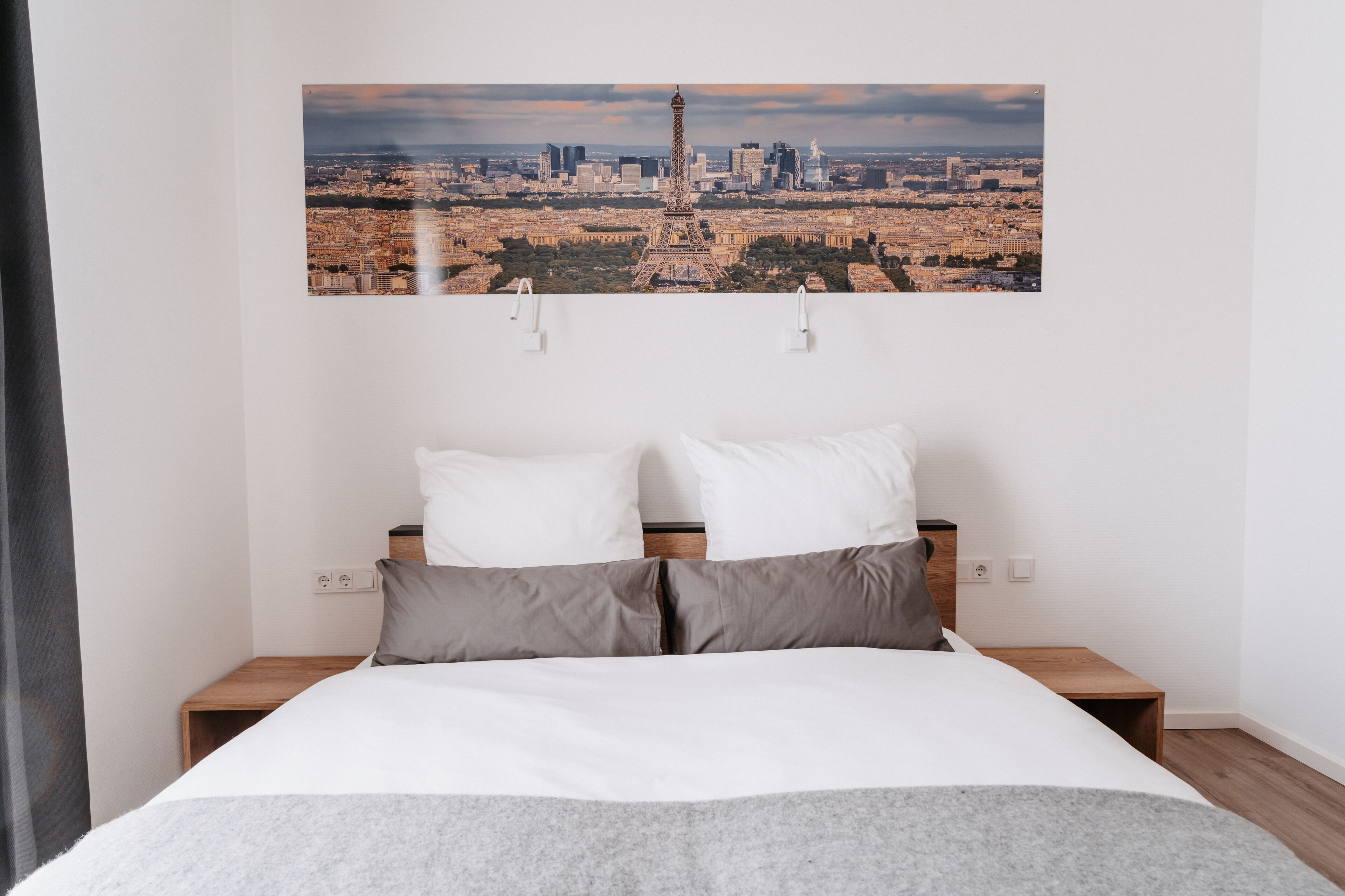 A hotel room with a bed, two bedside tables, and a large cityscape photo on the wall.