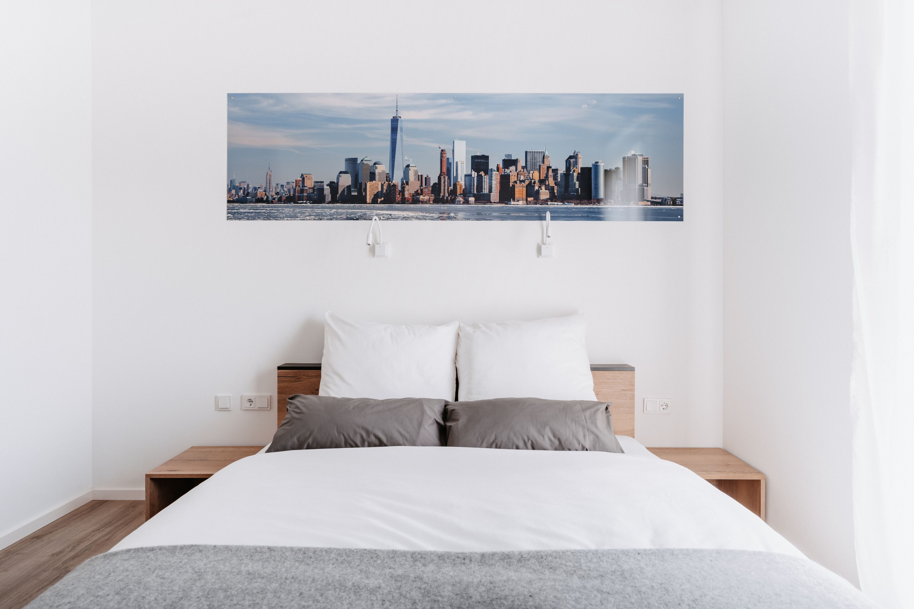 Una camera d'albergo con un letto, due comodini, vista sulla città e una parete bianca.