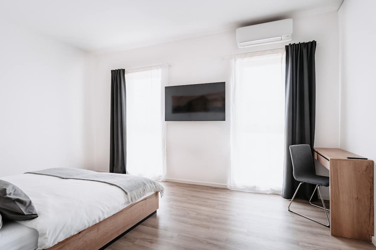 A modern bedroom with a bed, a desk, and a TV.