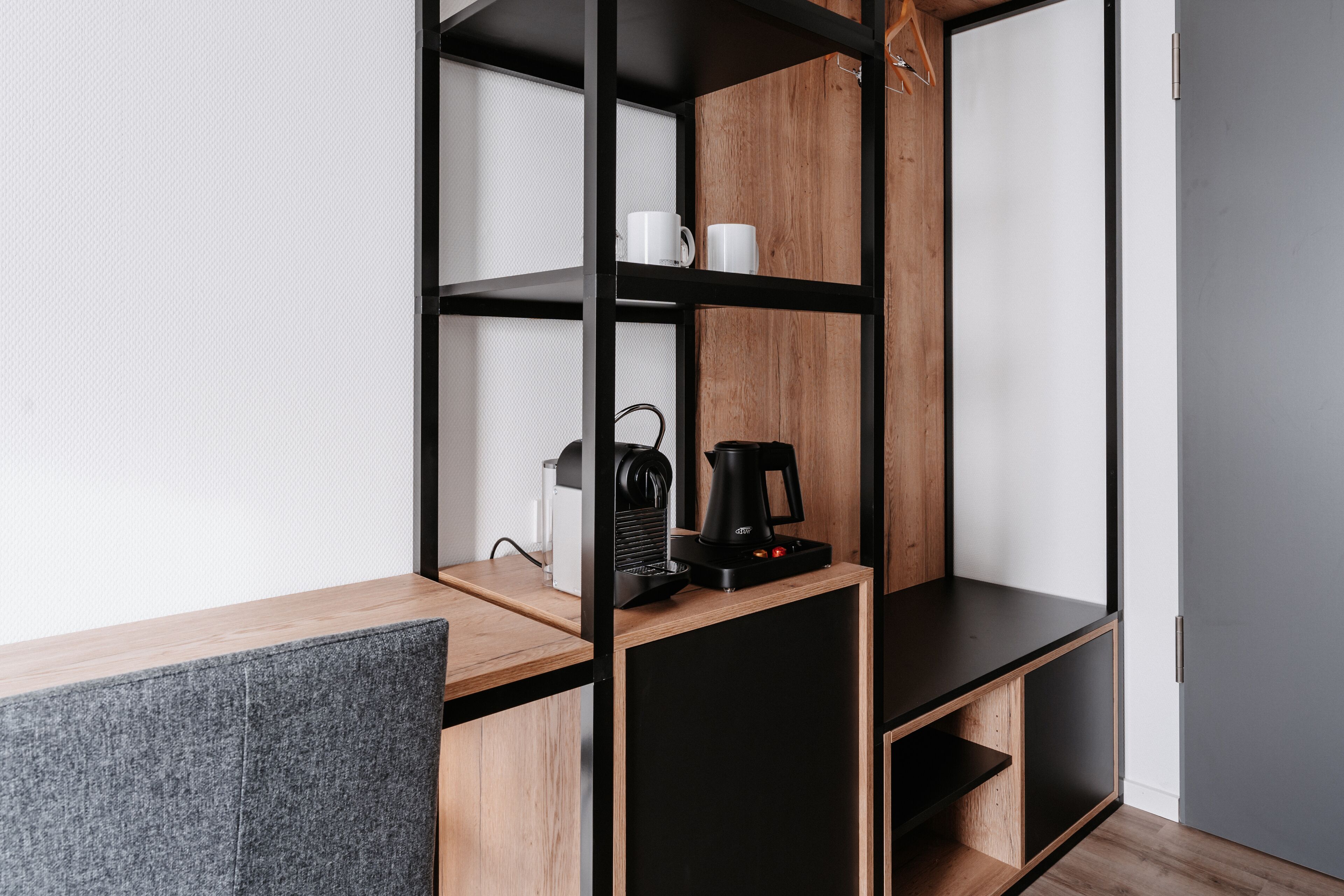 A modern room with a wooden desk, black shelving unit, and a coffee maker.
