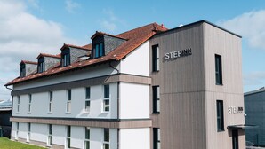 A modern building with a mix of white and grey exterior walls, a red-tiled roof, and the name "STEPPN" on the side. - Step Inn The Fair Hotel (Rosbach vor der Hoehe)