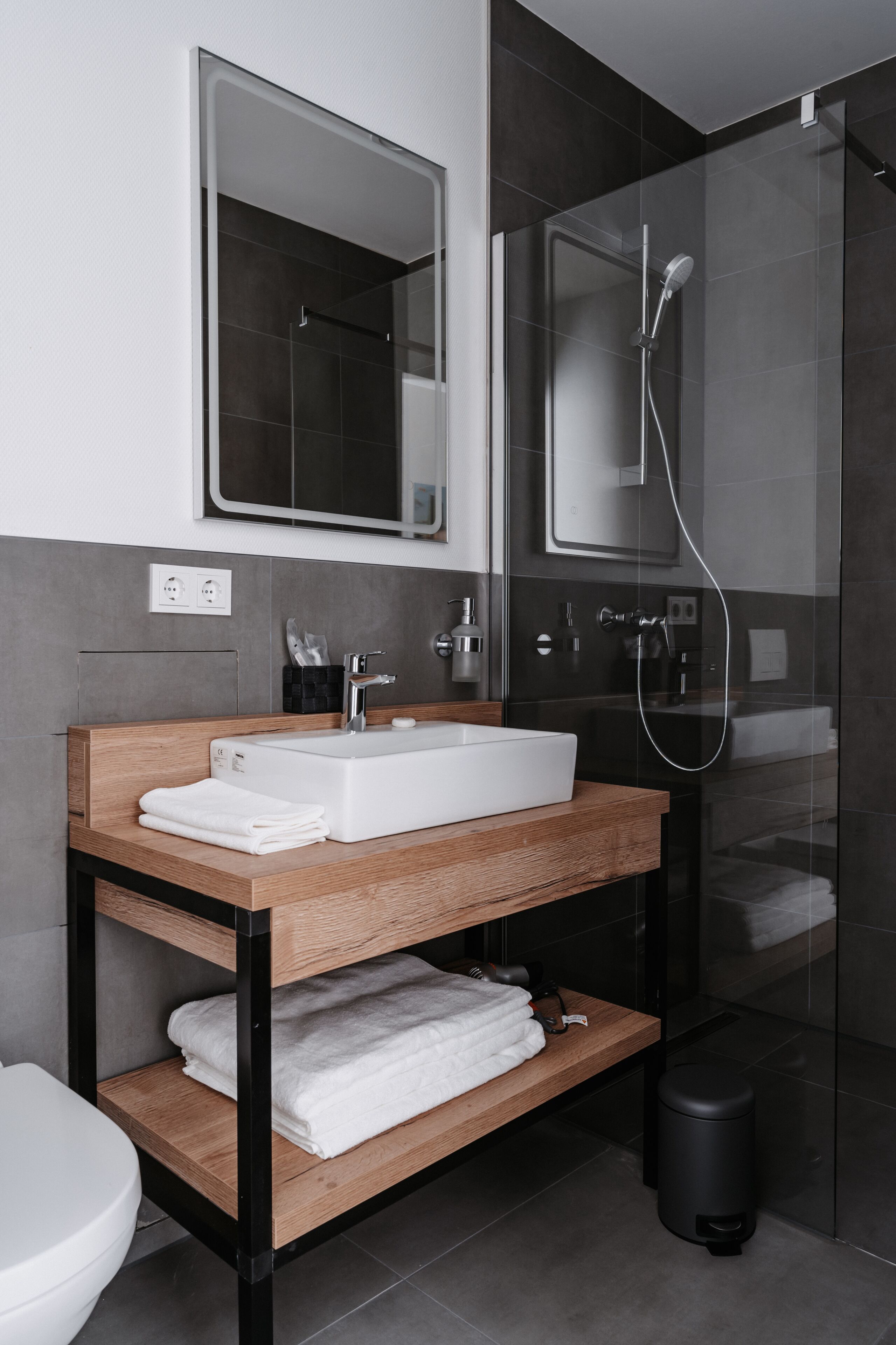 A modern bathroom with a wooden vanity, a white sink, a mirror, and a glass-enclosed shower.