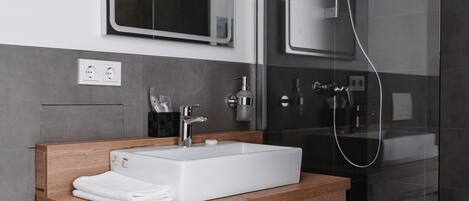 A modern bathroom with a wooden vanity, a white sink, a mirror, and a glass-enclosed shower.