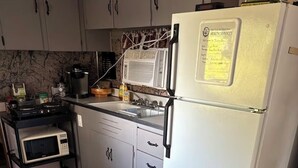 A compact kitchen with a white refrigerator, a microwave, a stove, and a sink.