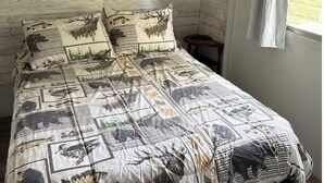 A bed with a patterned bedspread, a wooden headboard, and a window with curtains.