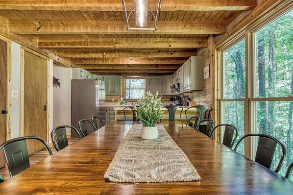A wooden dining table with chairs, a central plant, and a kitchen in the background. - Secluded, Views, and Close to Everything! (Sevierville)