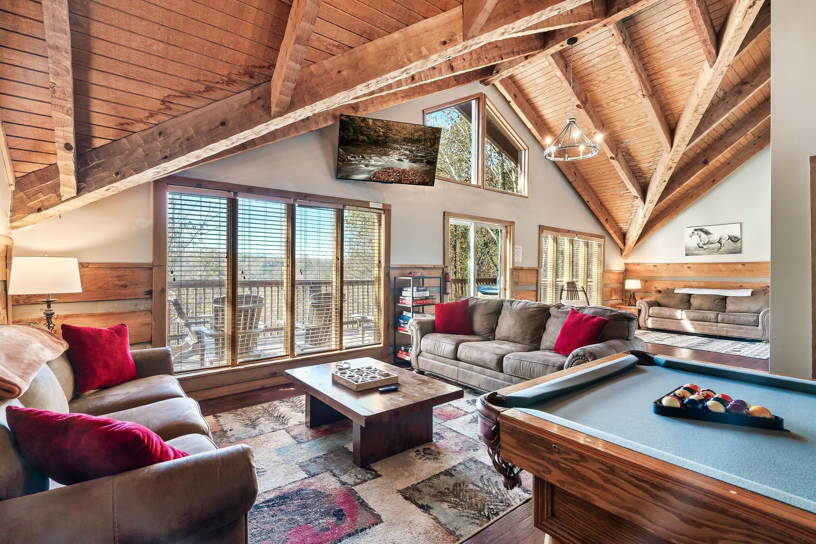 A spacious living room with a pool table, leather sofas, and large windows offering a view of the outdoors.