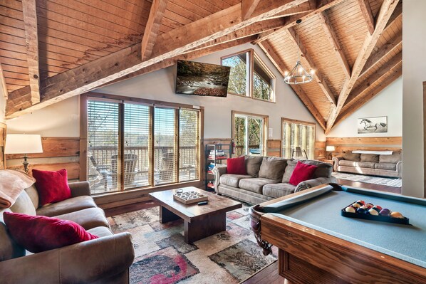 A spacious living room with a pool table, leather sofas, and large windows offering a view of the outdoors. - Secluded, Views, and Close to Everything! (Sevierville)