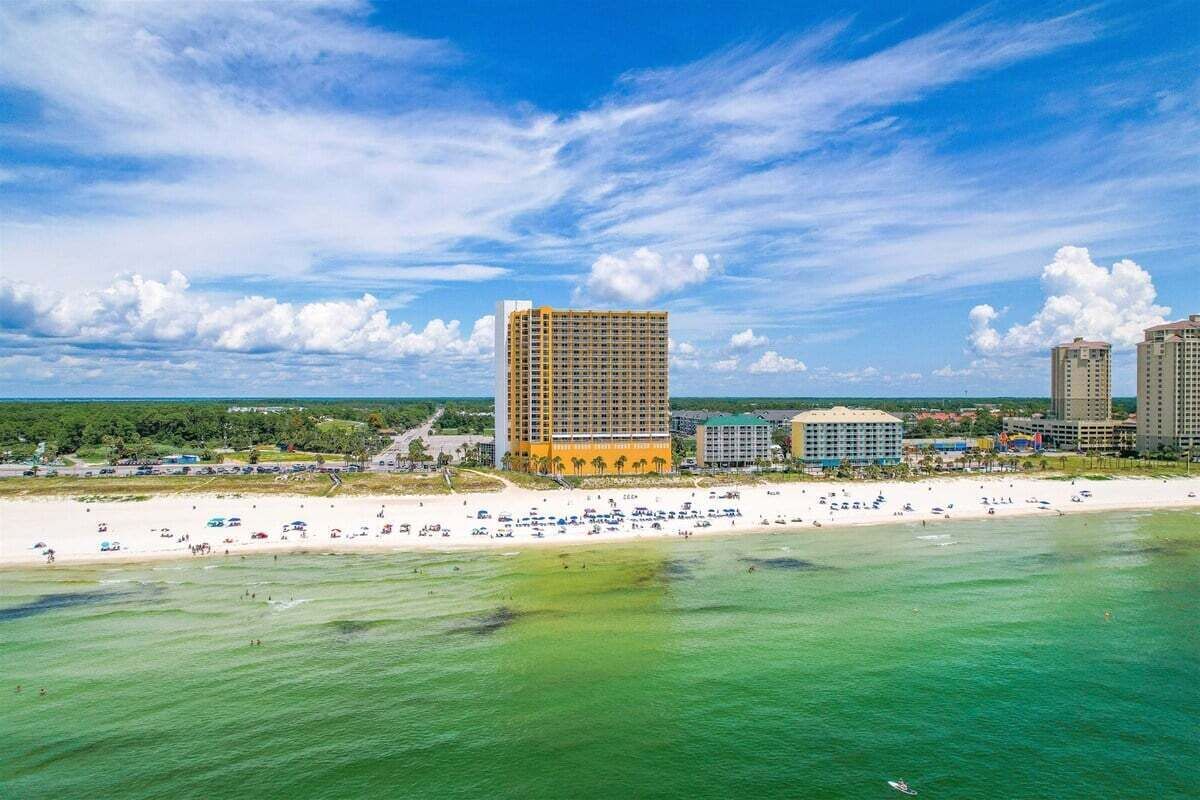 A coastal hotel with multiple buildings, a sandy beach, and clear blue skies.