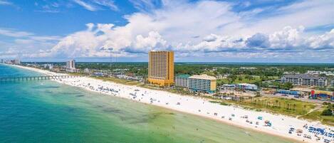 A coastal hotel with a beach view, a pier, and a large building in the background.