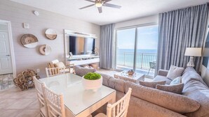 Ein modernes Wohnzimmer mit einem Glastisch, beigefarbenen Sofas, einem Flachbildfernseher und einem Balkon mit Blick.