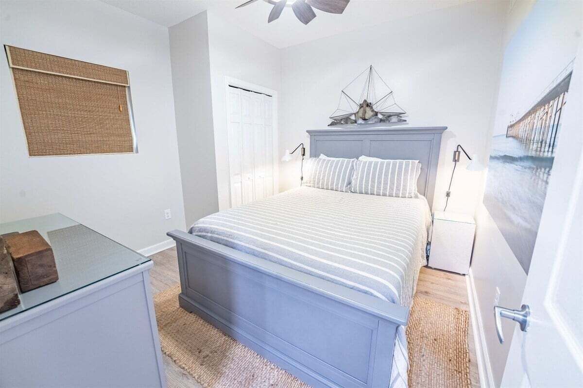 A bedroom with a bed, a nightstand, a desk, and a ceiling fan.
