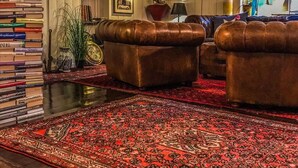 A cozy living room with leather sofas, a large red patterned rug, and a bookshelf filled with books.