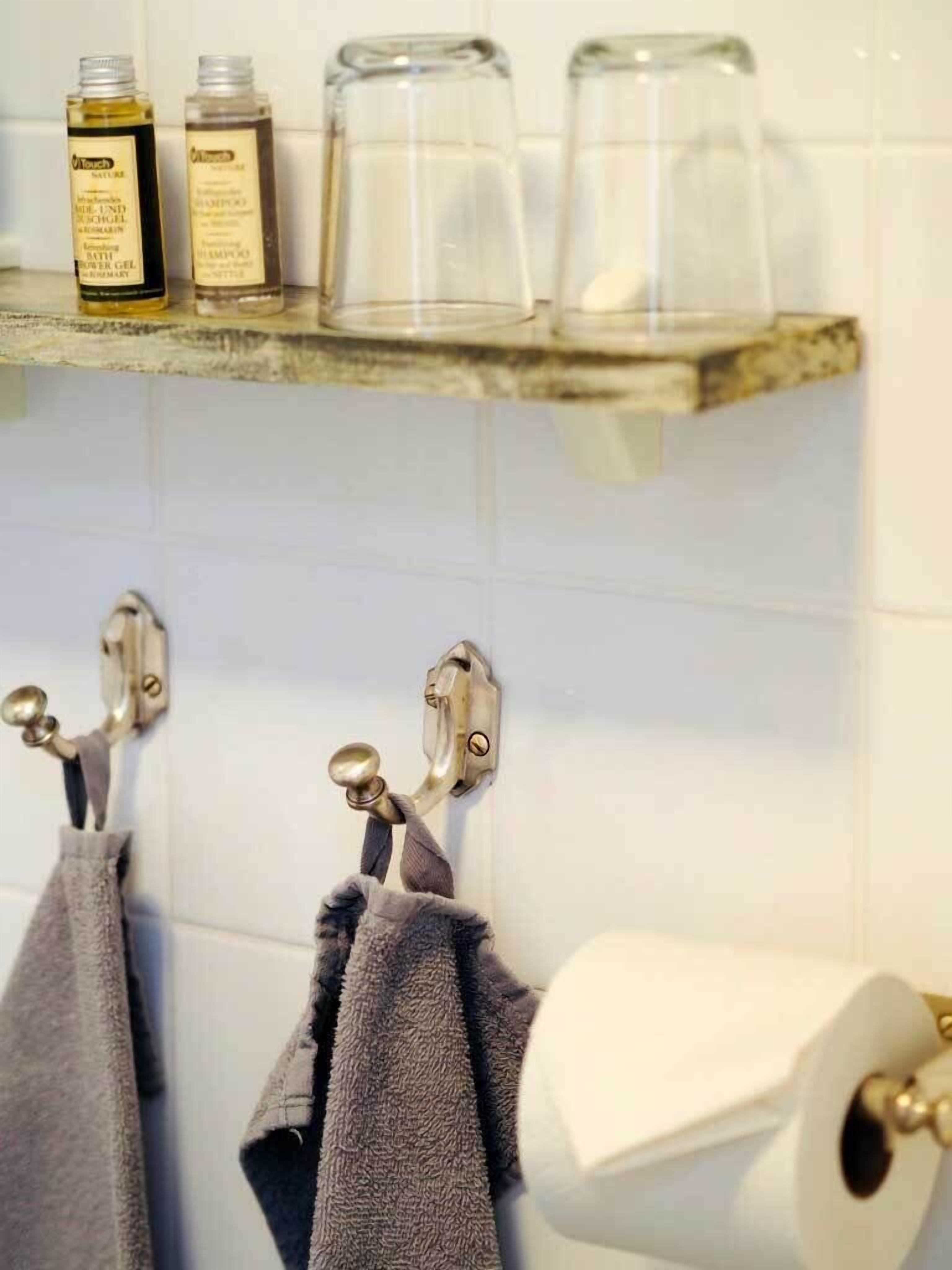 Une salle de bain avec une étagère où sont rangés les articles de toilette, des serviettes suspendues  à des crochets et un porte-rouleau de papier toilette.