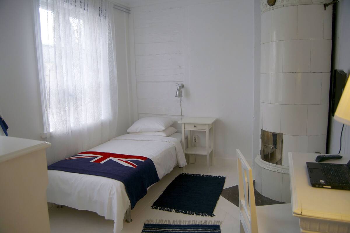Un dormitorio con una cama individual, una mesita de noche, una lámpara, una ventana con cortinas y un baño con inodoro y lavabo.