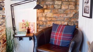 A cozy corner with a leather armchair, a plaid pillow, a small table with a lamp, and a bookshelf filled with books.