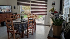 Comedor con mesa preparada para cuatro, sillas de madera, televisor y planta en maceta.