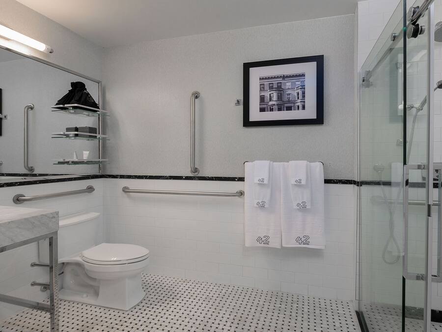 A modern bathroom with a toilet, bidet, and shower. There are handrails, a glass shower enclosure, and a framed picture on the wall.