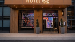 A hotel entrance with a neon sign, large glass windows, and two potted plants. - 42 Hotel (Brooklyn)