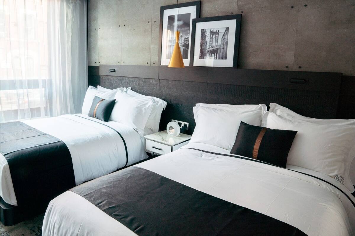 A hotel room with two beds, a nightstand, a vase, and framed pictures on the wall.