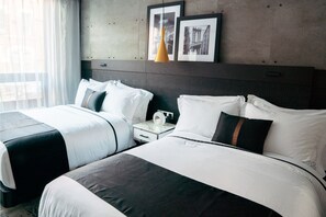 Ein Hotelzimmer mit zwei Betten, einem Nachttisch, einer Vase und gerahmten Bildern an der Wand.