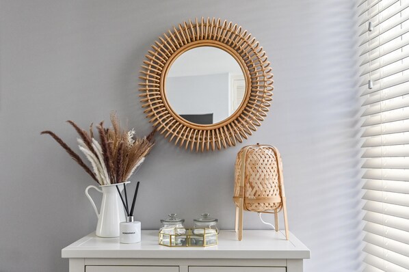 A white dresser with a mirror, a vase with pampas grass, and two glass jars.