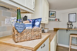 A kitchen counter with a wicker basket containing a bottle, a heart-shaped sign, a bag of chips, and a box.